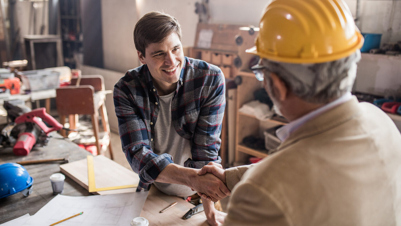 Young smiling carpenter shaking hand with quality control inspector in a workshop.